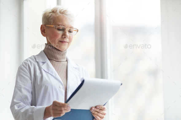 Portrait of Female Doctor Holding Clipboard by Window - Stock Photo - Images