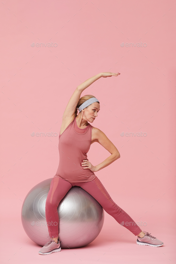 Active Mature Woman Stretching against Pink - Stock Photo - Images