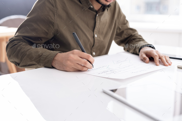 Young busy economist drawing flow chart on paper while preparing report - Stock Photo - Images