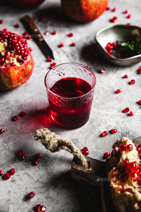 Red pomegranate juice in a glass, ripe and cut pomegranate and a sprig of mint on a gray background - Stock Photo - Images