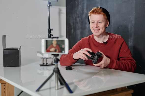 Young cheerful man in casualwear presenting his new photocamera in studio - Stock Photo - Images