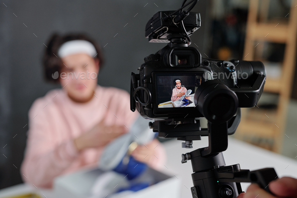 Young vlogger in casualwear showing sneakers on display of digital video camera - Stock Photo - Images