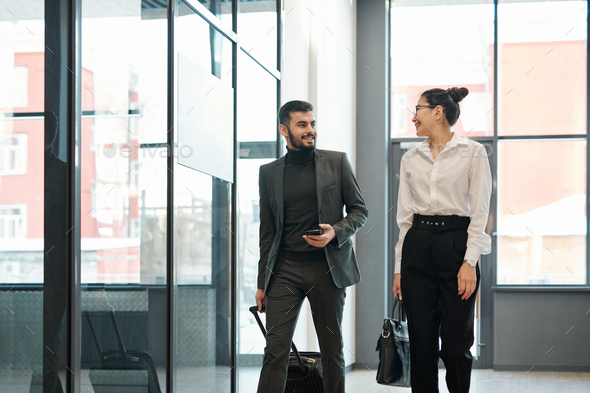 Two young intercultural business colleagues on travel moving along airport - Stock Photo - Images