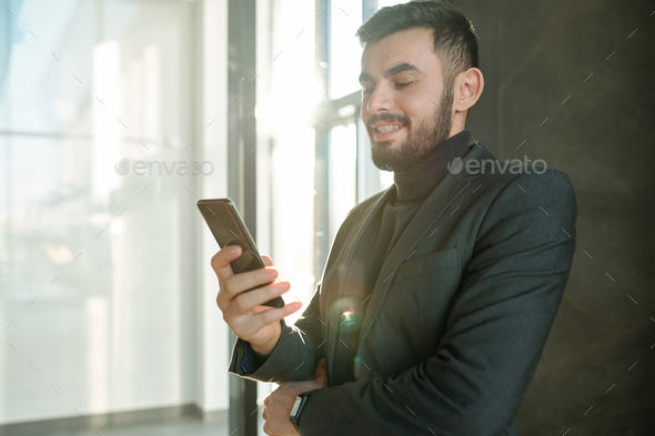 Happy young businessman scrolling in smartphone and looking through contacts - Stock Photo - Images