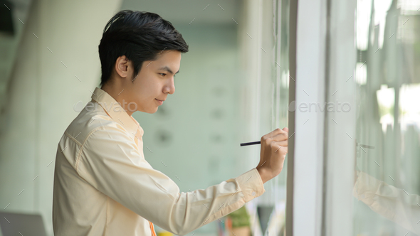 Young business man is taking notes working on a note on a glass wall in a modern office.