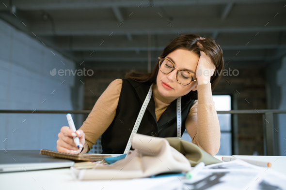 Young pensive female designer thinking over new fashion sketch in studio - Stock Photo - Images