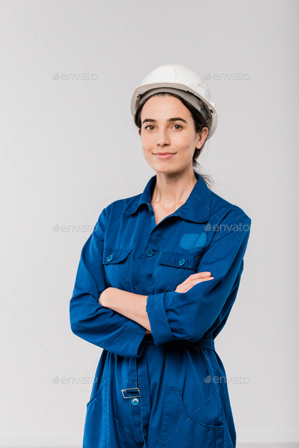 Pretty young cross-armed female engineer in blue workwear and safety helmet - Stock Photo - Images