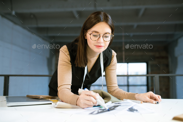 Creative young female designer pointing at on of fashion sketches at work - Stock Photo - Images