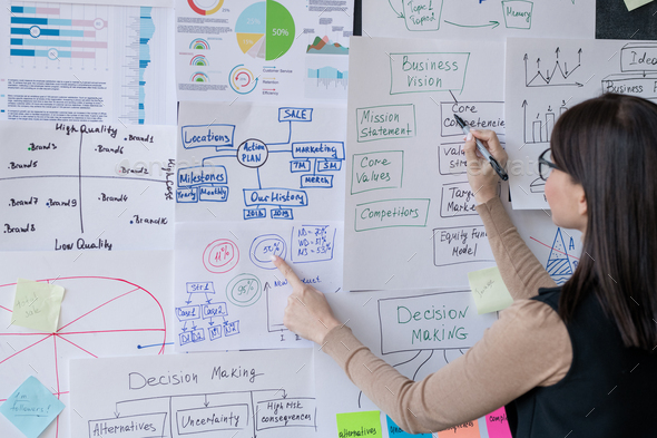 Young financial analyst pointing at papers with charts on blackboard - Stock Photo - Images
