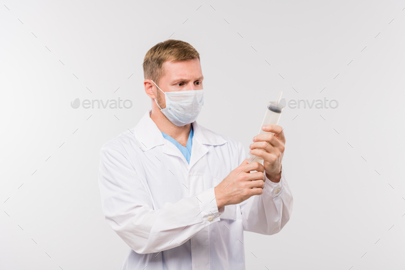 Young male clinician in whitecoat and protective mask holding big syringe - Stock Photo - Images