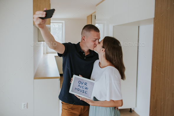 Young couple kissing and taking selfie in new house.
