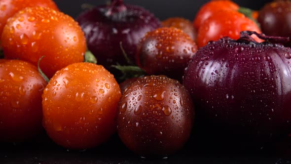 Cherry tomatoes, cucumbers, avocado and red onion on a black background in water drops. alt