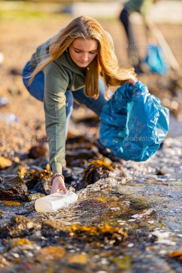 Young woman picking up garbage from rocky shore - Stock Photo - Images