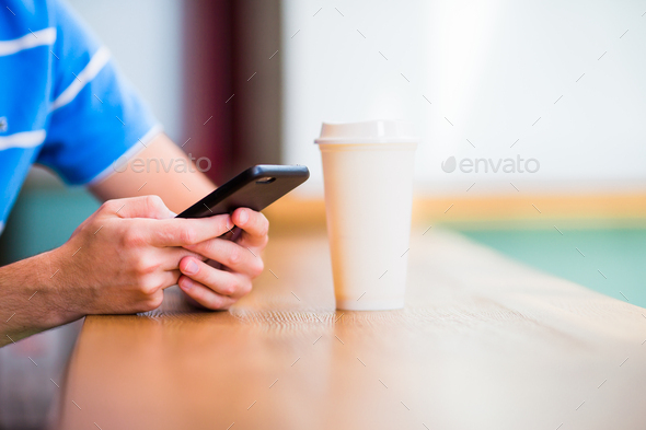 Closeup of male hands holding cellphone and class of cofee in cafe. Man using mobile smartphone - Stock Photo - Images