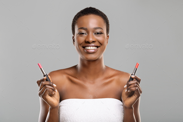 Black woman choosing between two lipstick colors, red and pink - Stock Photo - Images