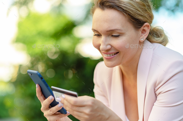 Businesswoman with a credit card and phone makes purchasing outdoors. - Stock Photo - Images