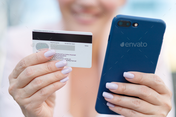 Businesswoman with a credit card and phone makes purchasing outdoors. - Stock Photo - Images
