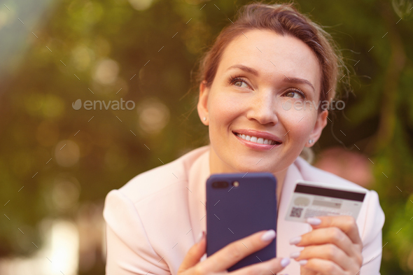 Businesswoman with a credit card and phone makes purchasing outdoors. - Stock Photo - Images