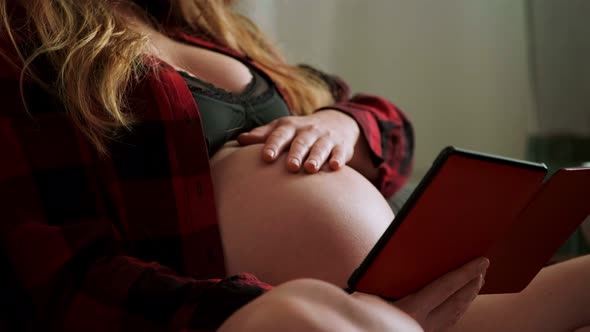 Pregnant woman reading e-book sitting on couch