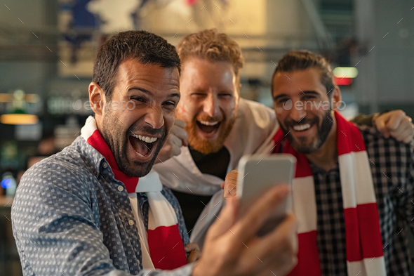 Excited supporters watching football match on phone - Stock Photo - Images