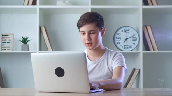 Smiling Boy in Chatting Online By Video Call with Laptop Computer at Home While Sitting at the Table alt