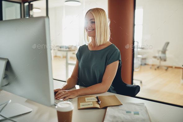 Smiling businesswoman working at her office desk in the afternoon - Stock Photo - Images