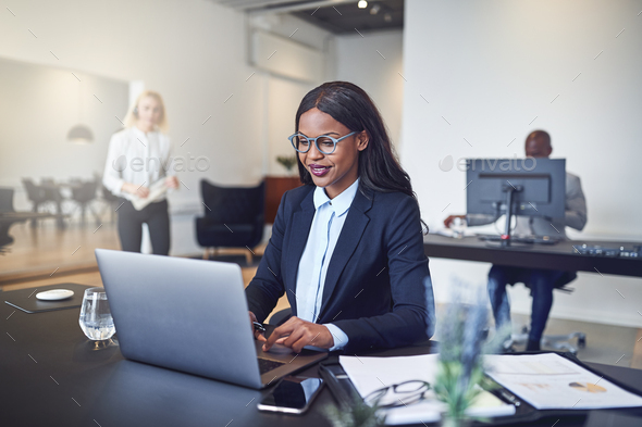 Smiling African American businesswoman sitting at work using a laptop - Stock Photo - Images