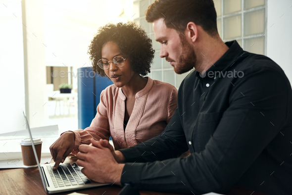 Two diverse colleagues using a laptop in a modern office - Stock Photo - Images