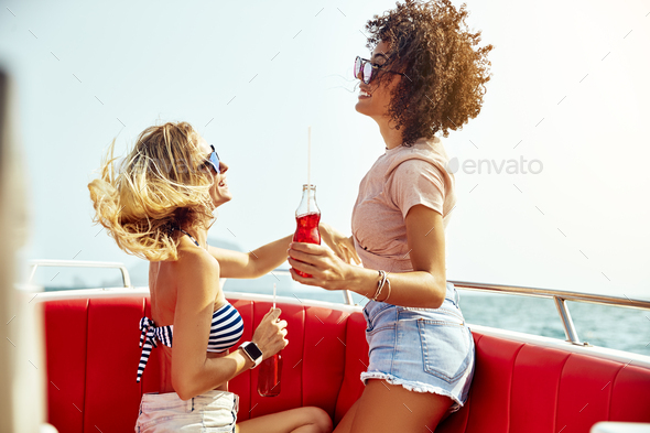 Two smiling young women enjoying drinks together on a boat - Stock Photo - Images
