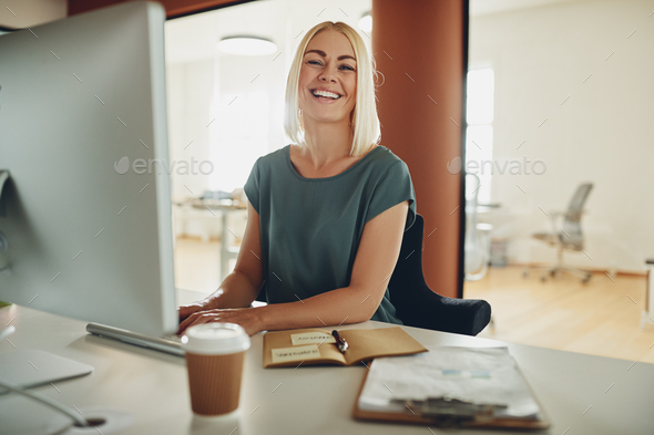 Young businesswoman laughing while working at her office desk - Stock Photo - Images