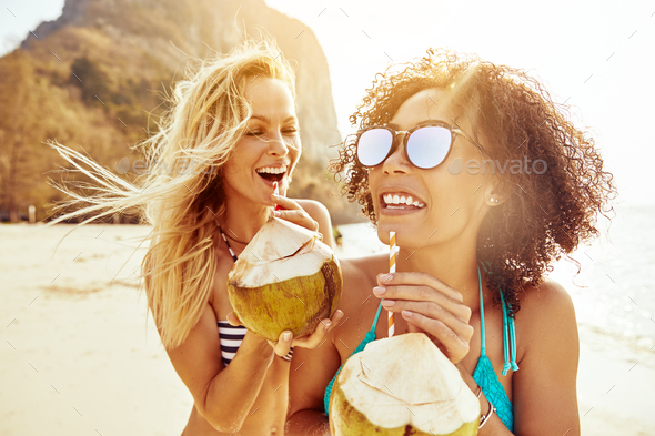 Laughing friends in bikinis drinking from coconuts on a beach - Stock Photo - Images