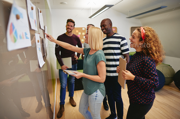 Smiling work colleagues reading paperwork together on an office wall - Stock Photo - Images