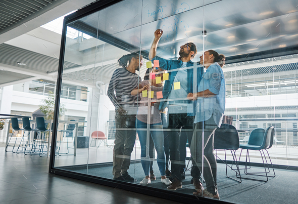 Diverse businesspeople brainstorming together on a glass wall - Stock Photo - Images