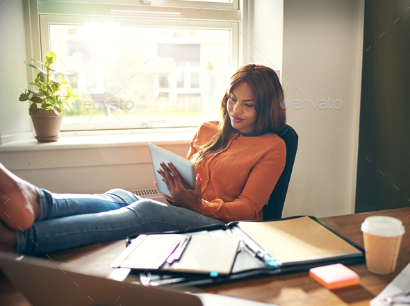 Smiling woman leaning back in her office chair working online - Stock Photo - Images
