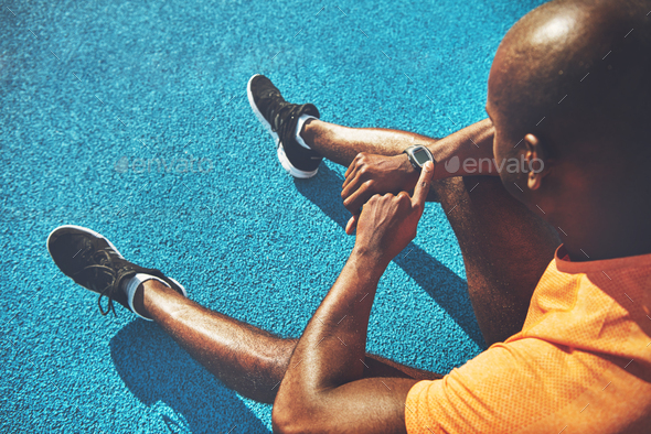Young runner sitting on a track checking his fitness watch - Stock Photo - Images