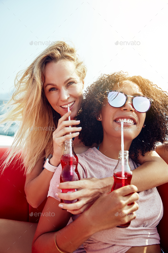 Two smiling young women sitting on a boat sipping drinks - Stock Photo - Images
