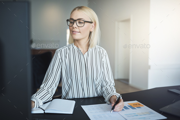 Smiling businesswoman working at her desk in a bright office - Stock Photo - Images