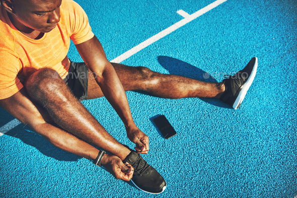 Young runner sitting on a track tying up his shoes - Stock Photo - Images