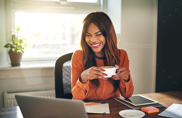 Laughing young woman drinking coffee while working from home - Stock Photo - Images