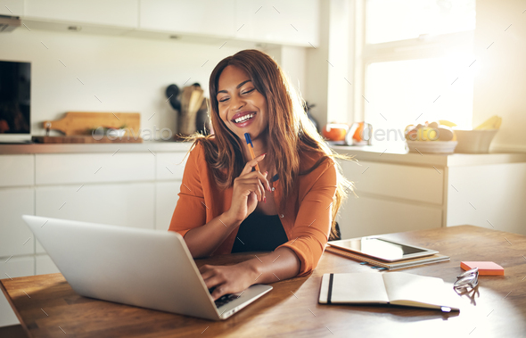Smiling woman working online at her kitchen table at home - Stock Photo - Images