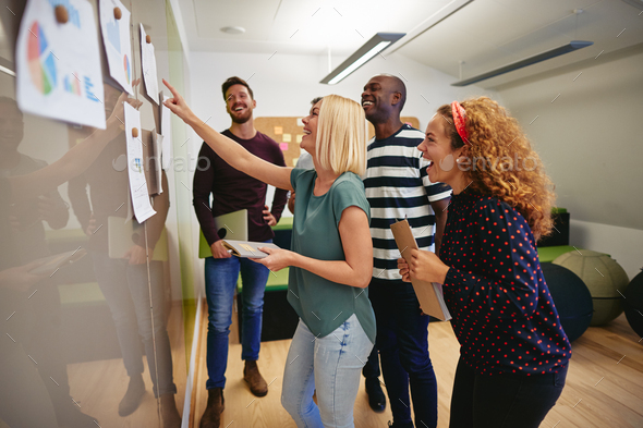 Laughing work colleagues discussing paperwork together on an office wall - Stock Photo - Images