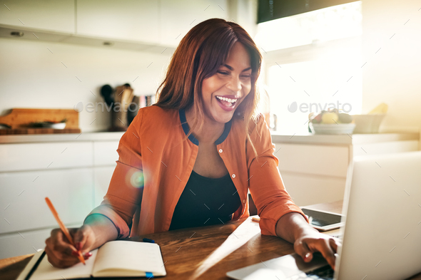 Laughing young female entrepreneur working online in her kitchen - Stock Photo - Images