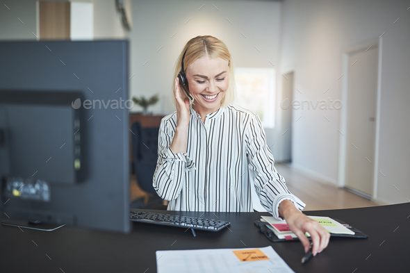 Smiling businesswoman talking on a headset at her office desk - Stock Photo - Images