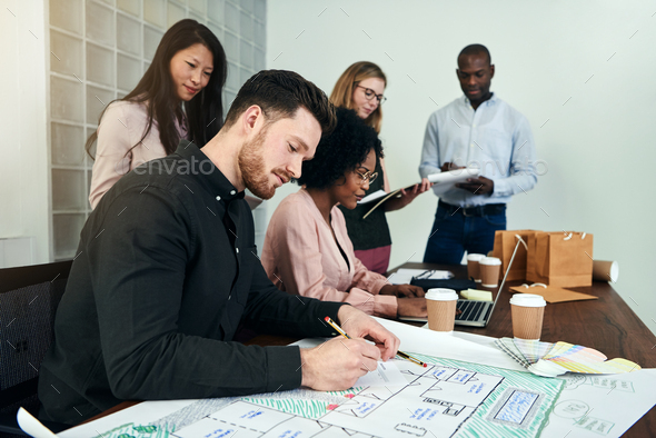 Male architect working on blueprints with colleagues in an office - Stock Photo - Images