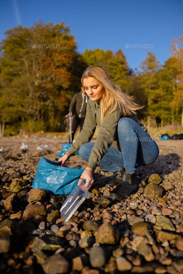 Young woman picking up plastic at rocky beach - Stock Photo - Images