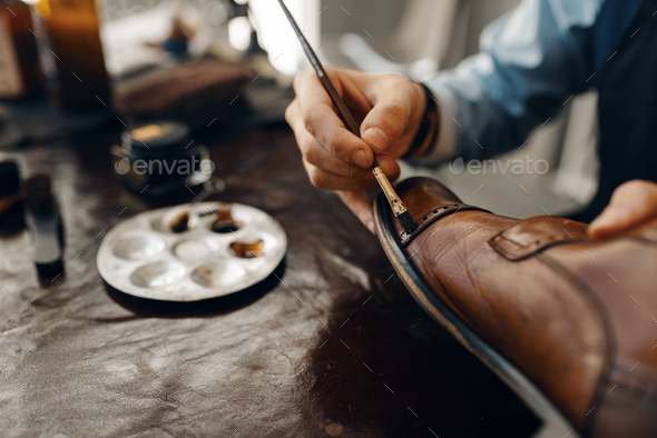 Shoemaker with brush tints shoes, footwear repair - Stock Photo - Images