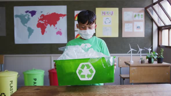 Boy wearing face mask holding recycle container in class at school  alt