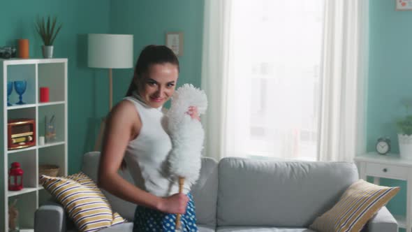 Young Woman Housekeeper Is Dancing with Fluffy Dust Brush