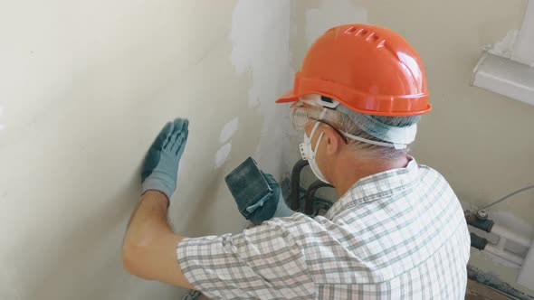 An Elderly Man Master Levels a Wall with a Tool in an Orange Helmet and Protective Glasses While