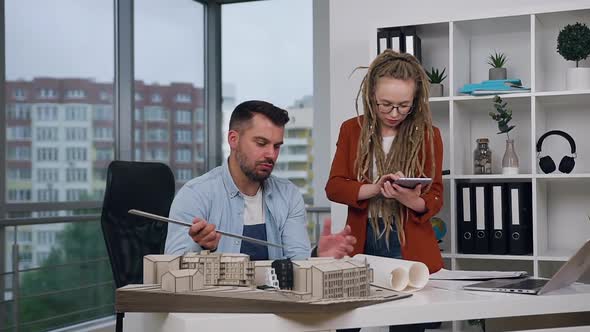 Man and Woman with Dreadlocks Working Together with Mock-up of New Buildings  alt
